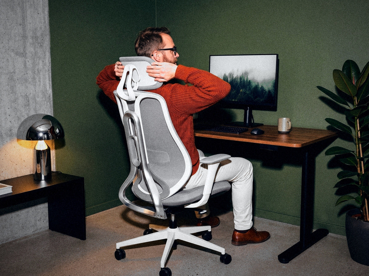 Vyras, sėdėdamas Ergonix OmniSit Pro kėdėje, reguliuoja galvos atramą, vaizdas iš nugaros